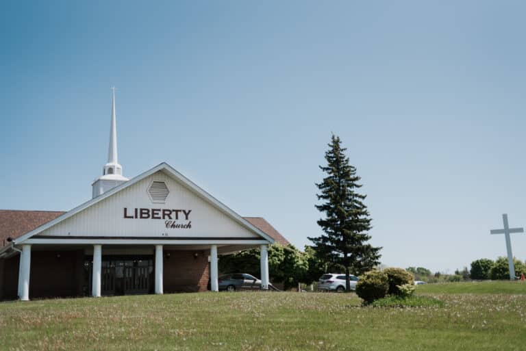 Wide shot of the front of the church building showing a tree and a cross on the front lawn