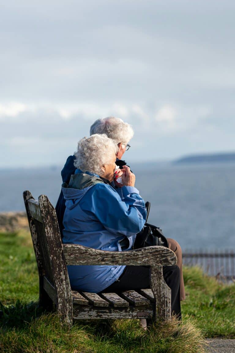 Two seniors sitting on a park bench overlooking a lake
