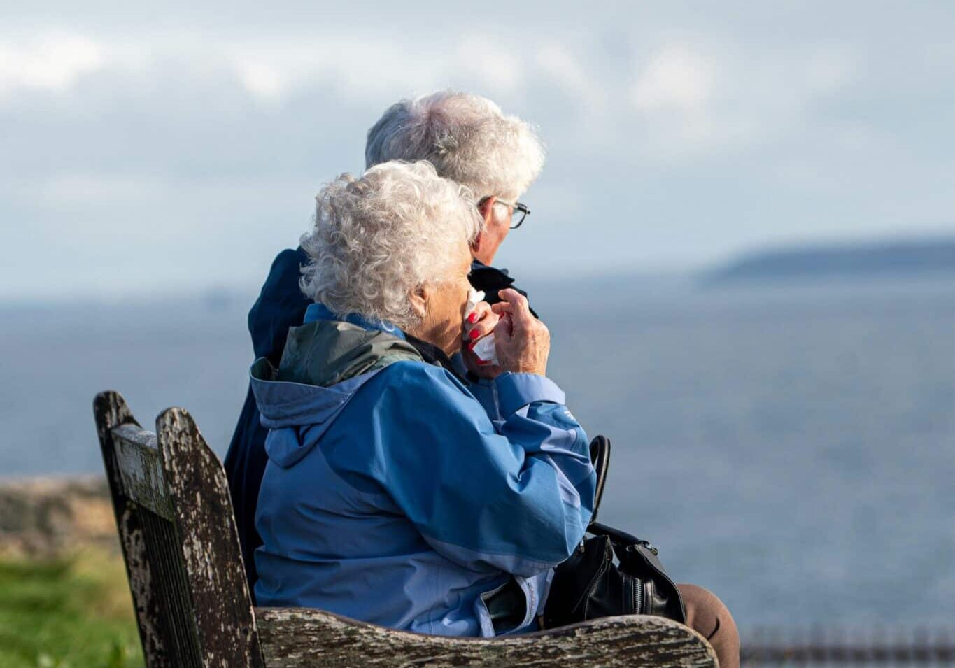 Two seniors sitting on a park bench overlooking a lake